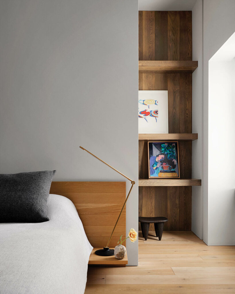 a white bed with a wood headboard near a minimalist lamp