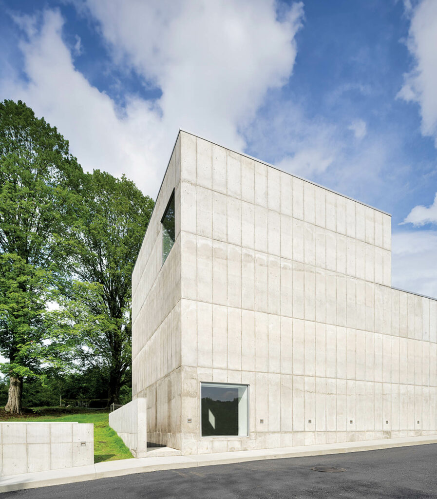 The facade of a cream blocklike structure surrounded by trees